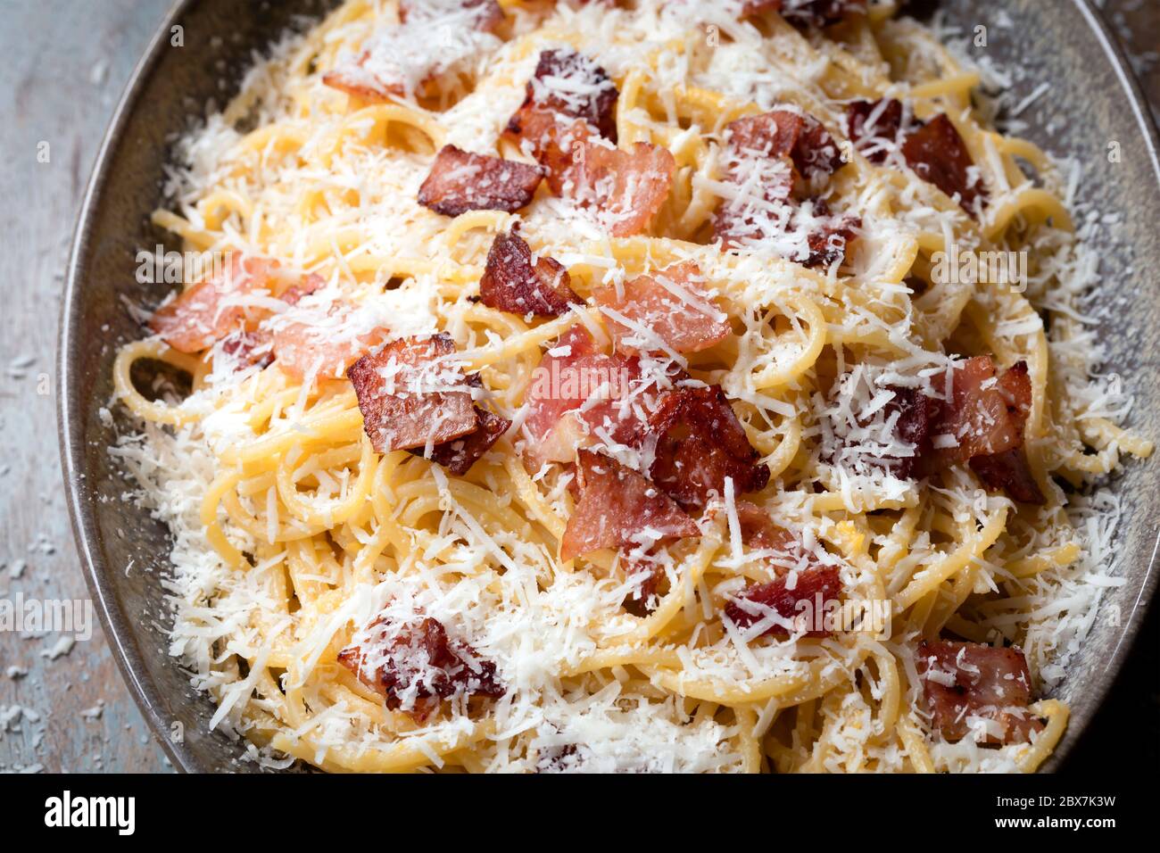 Spaghetti carbonara, top view, in oval dish on rustic timber table. Stock Photo