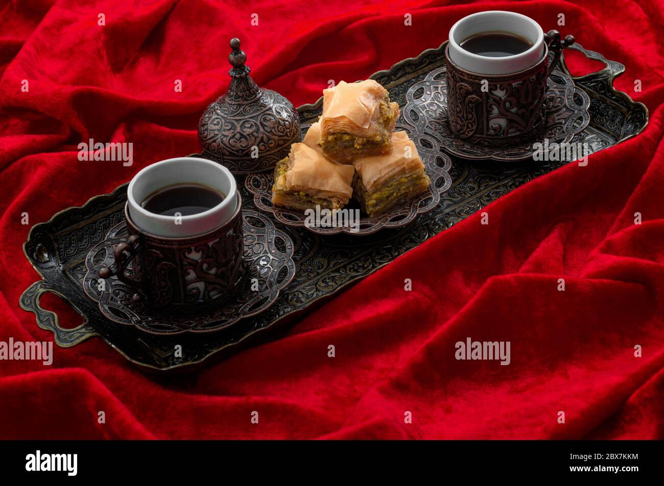 Ramadan treat and arabian hospitality concept with turkish baklava and mini coffee cups on authentic mediterranean metal tray isolated on red velvet f Stock Photo