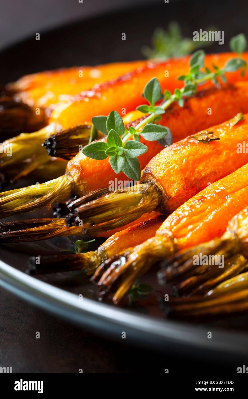 Roasted baby carrots with thyme, in black serving dish Stock Photo Alamy