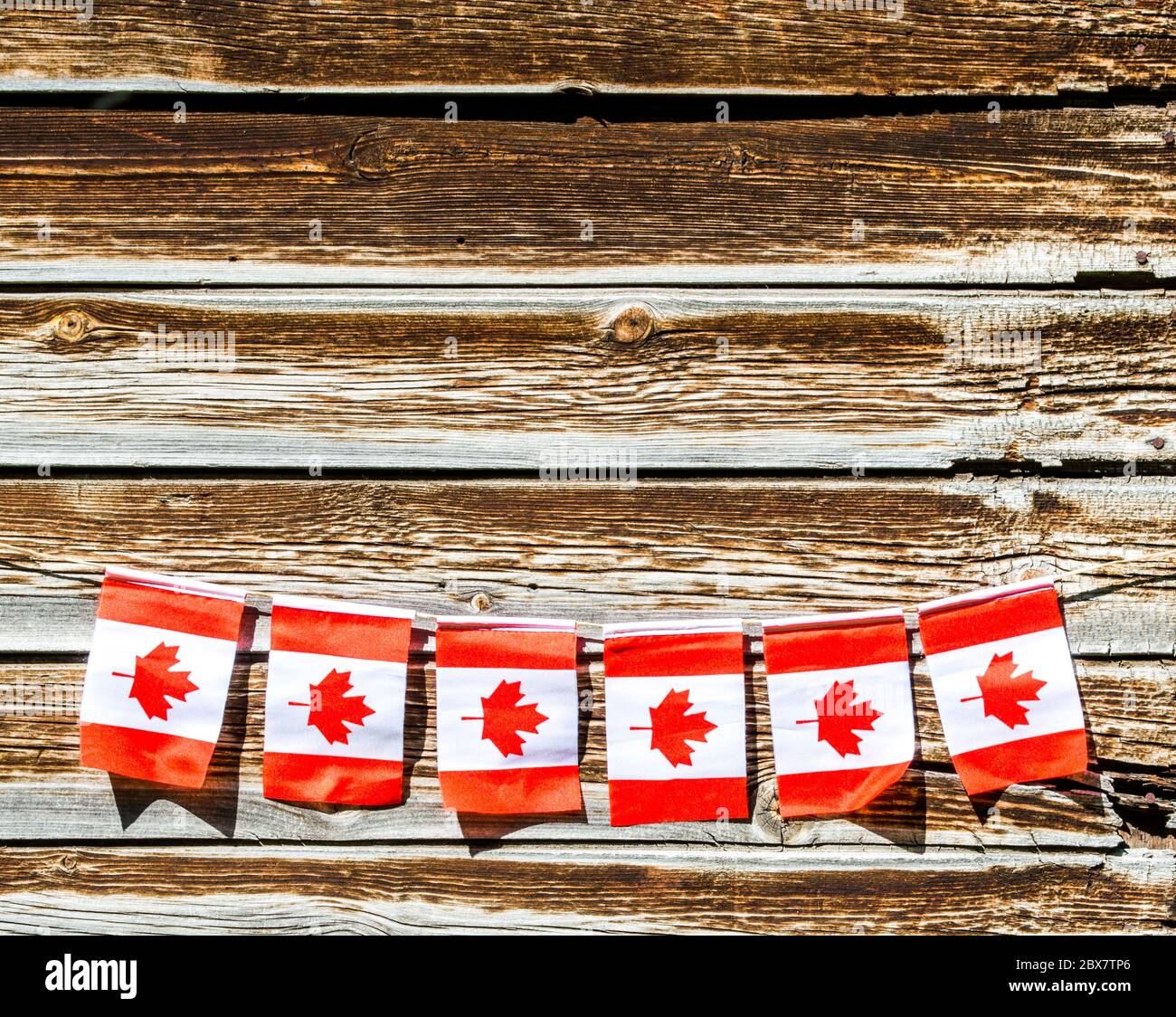 miniature Canadian flags strung along a rope on the exterior wall of an old barn with copy space Stock Photo