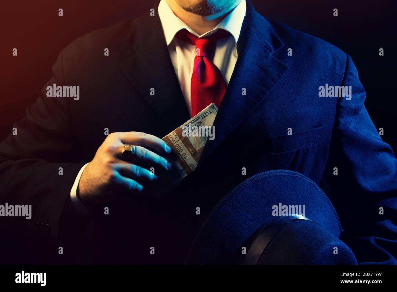 Mafia man in black suit, red tie putting money in pocket on black background. Stock Photo