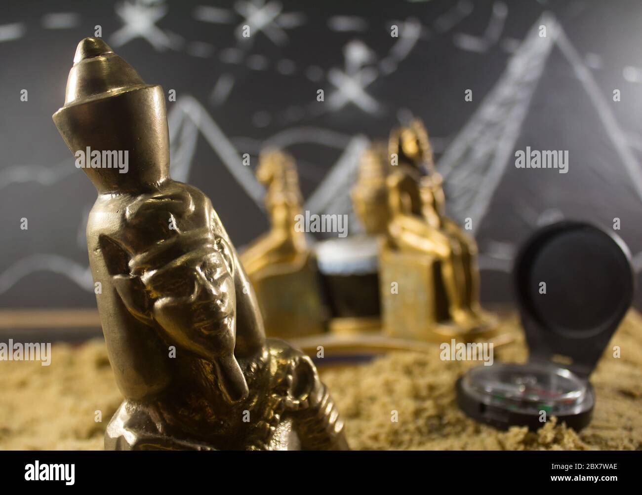 Ancient old pharaoh closeup metal statuettes standing on a sand surface with a blackboard drawn background & compass. Stock Photo