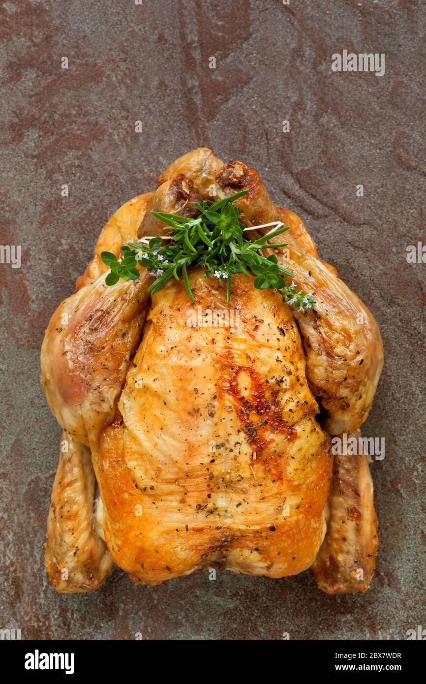 Roast chicken with fresh herbs. Overhead view, on rustic stone
