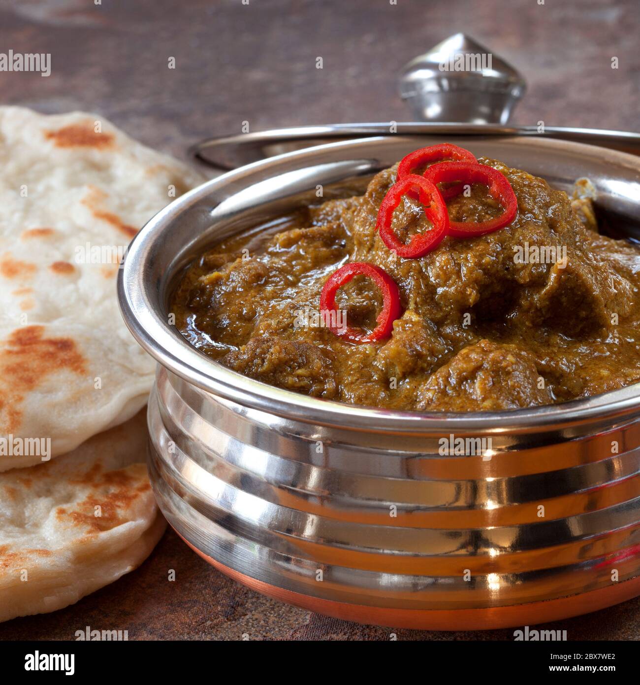 Indian lamb korma curry in traditional copper bowl, with naan bread