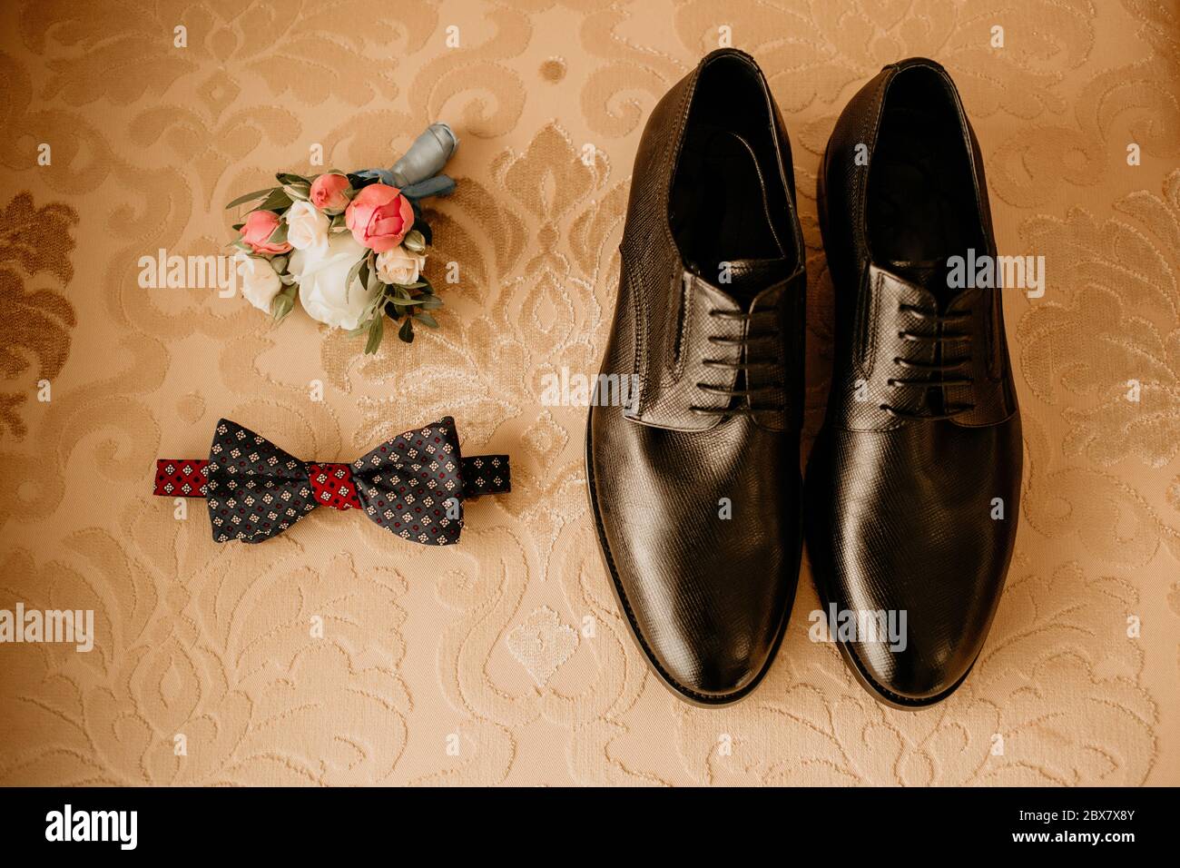 Close up of modern groom accessories. Black bowtie, leather shoes and flower boutonniere on rustic background. Set for formal style of wearing isolate Stock Photo