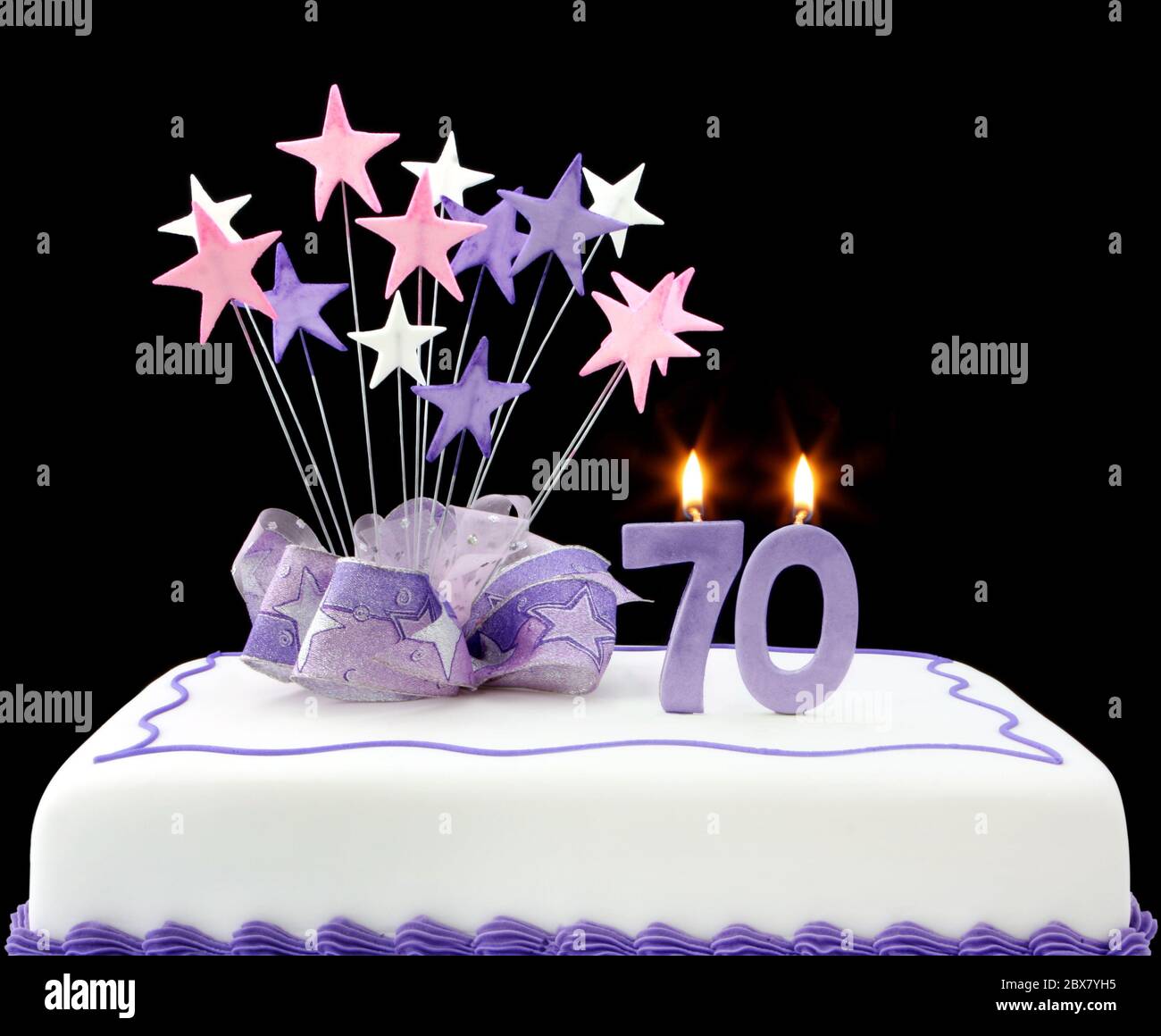 Fancy cake with number 70 candles.  Decorated with ribbons and star-shapes, in pastel tones on black background. Stock Photo