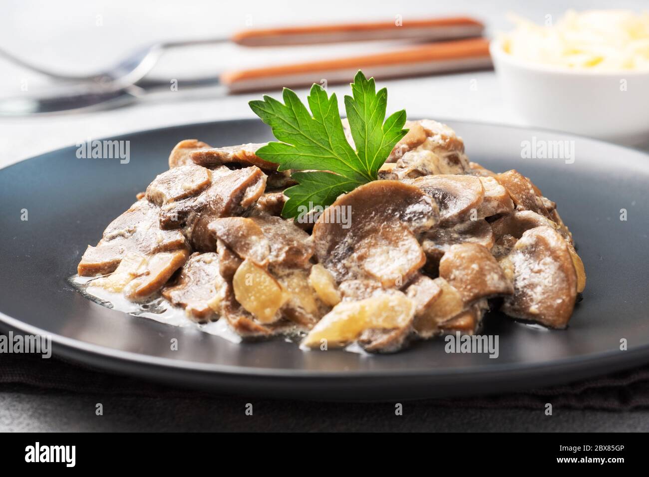 Stewed mushrooms champignons in sauce with sour cream and cheese parsley on a plate Stock Photo