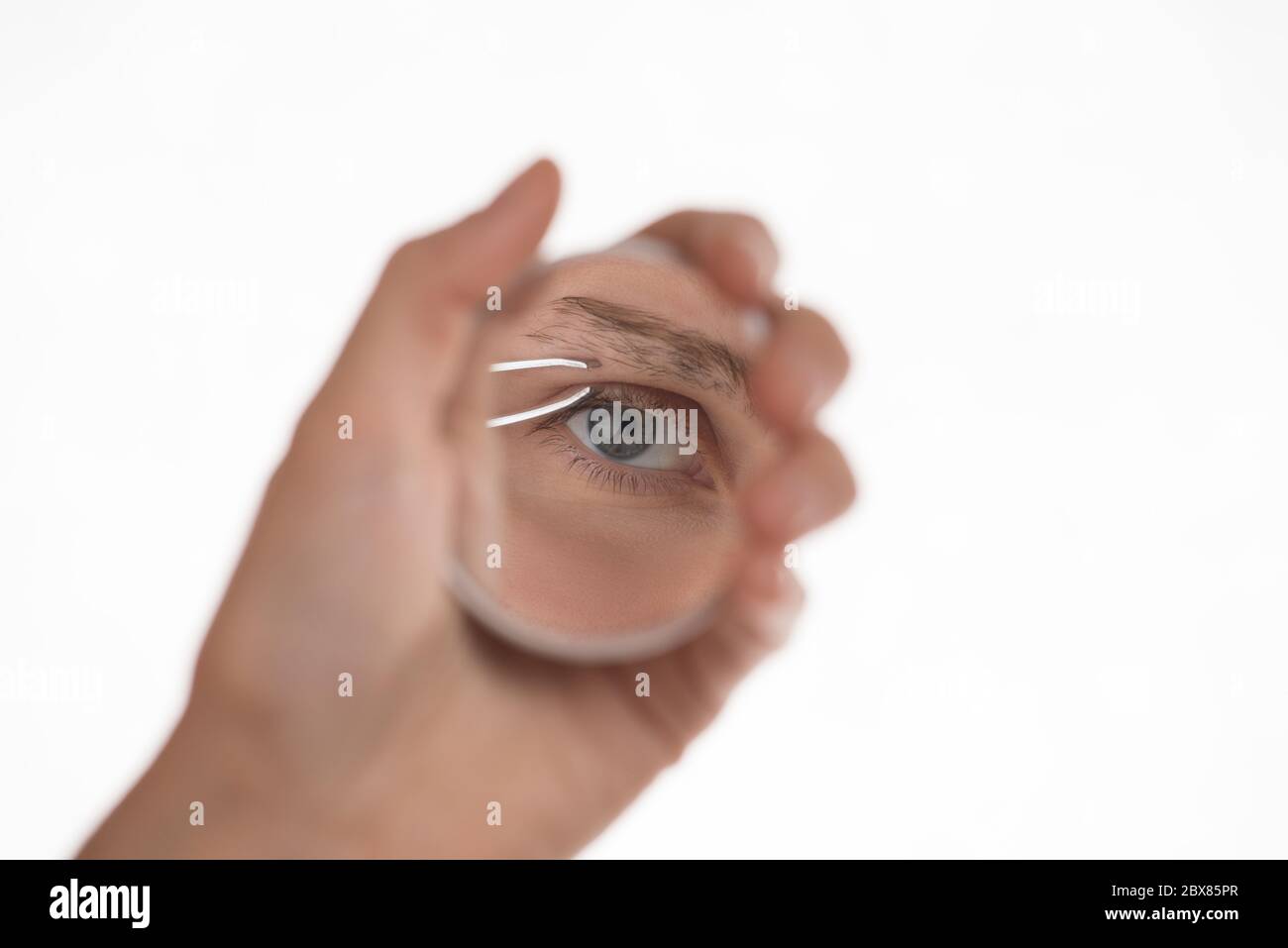 Young beautiful girl pulls out her eyebrows with tweezers metal on a white background Stock Photo