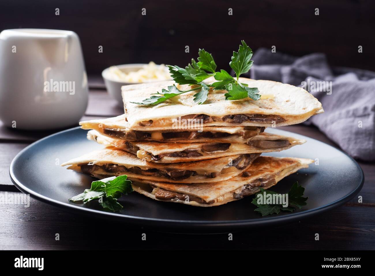 Pieces of quesadilla with mushrooms sour cream and cheese on a plate with parsley leaves. Wooden background close up Stock Photo