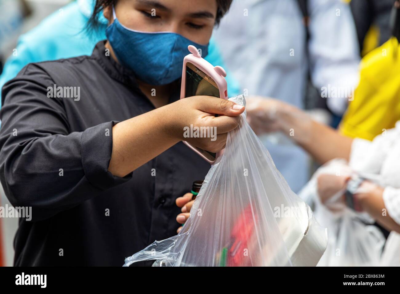 Lady with face mask receiving plastic bag full of free food during Covid pandemic, Bangkok, Thailand Stock Photo