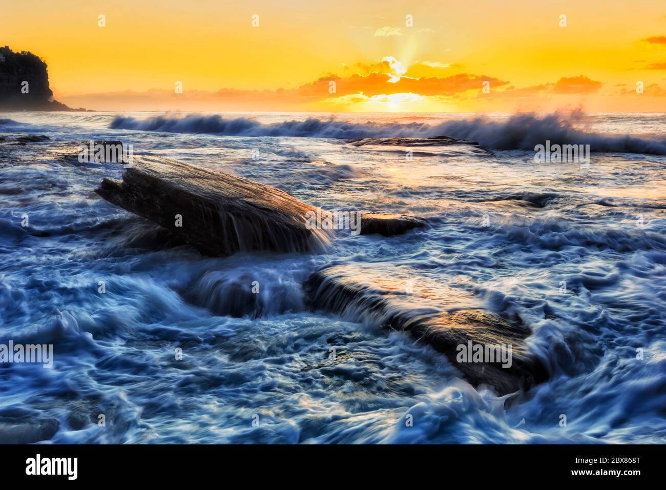 Colourful orange sunrise over Pacific ocean horizon off Northern beaches in Sydney during stormy weather. Stock Photo