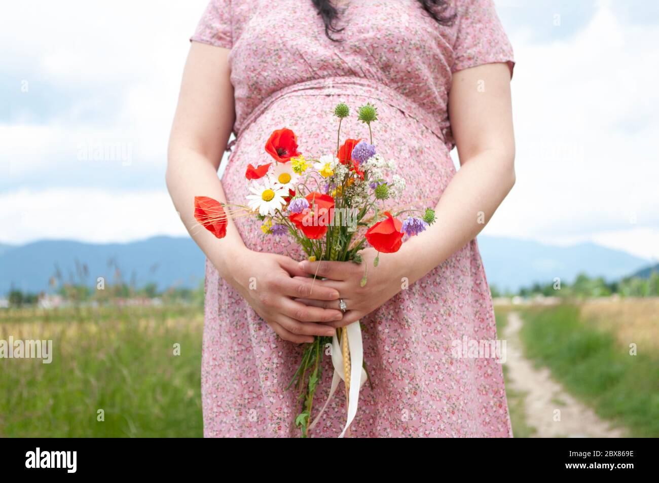 Stomach of the pregnant woman in a summer dress on the road outdoors