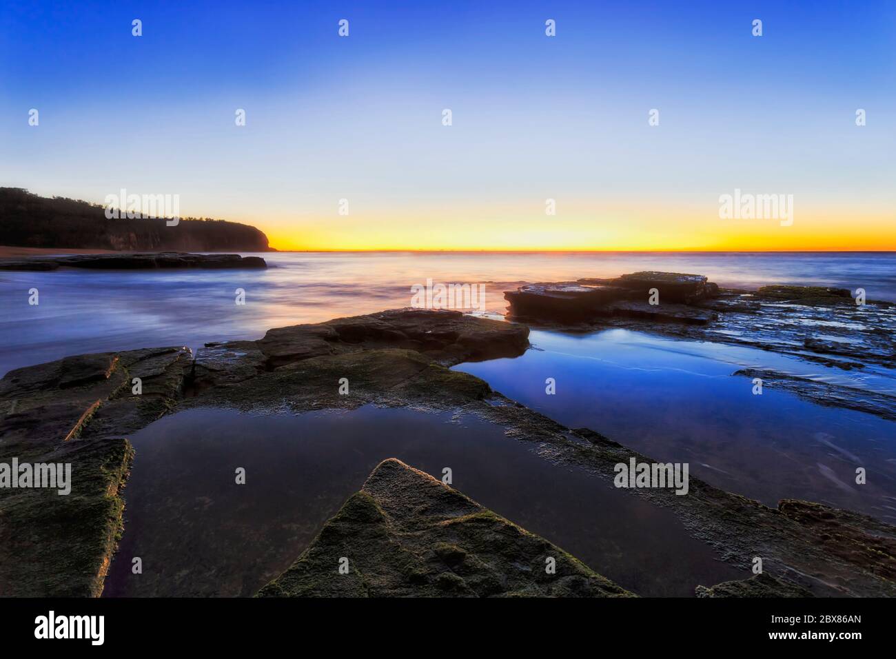 Seaweed covered sandstone plateau at Sydney Northern beach at sunrise facing Pacific ocean horizon. Stock Photo