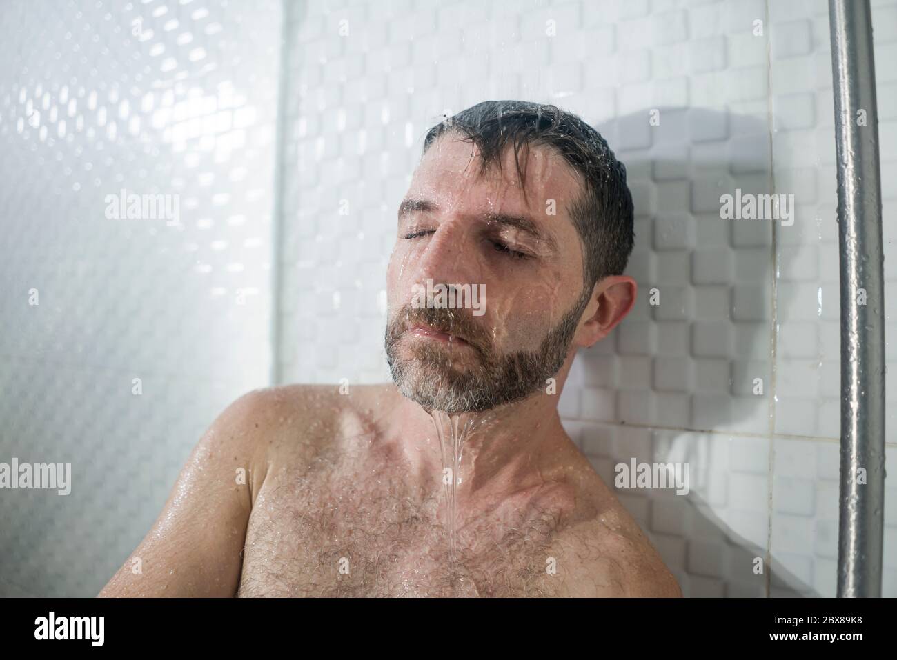 home bathroom dramatic portrait of young attractive sad and depressed man in the shower leaning