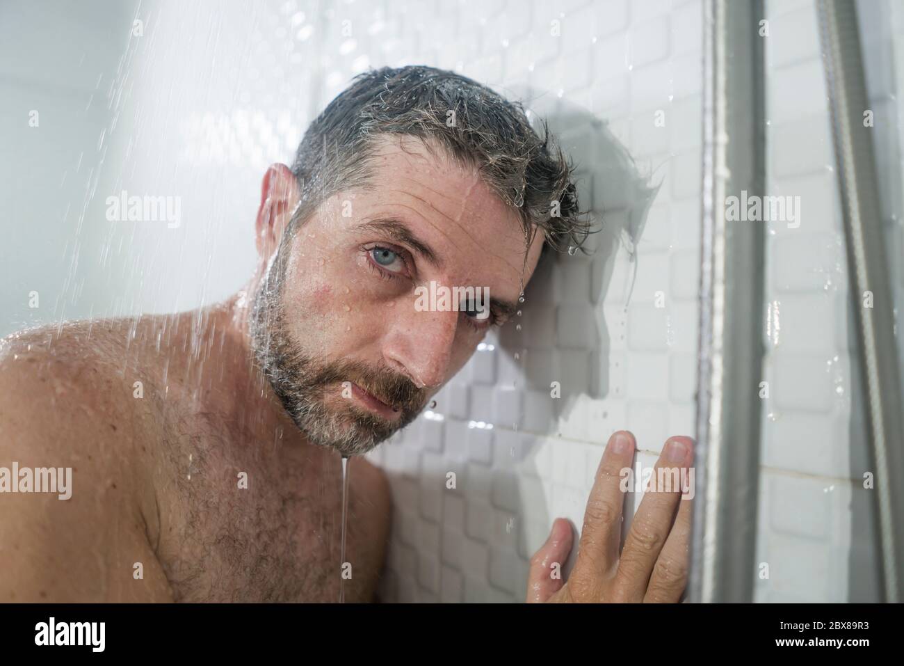 home bathroom dramatic portrait of young attractive sad and depressed man in the shower leaning
