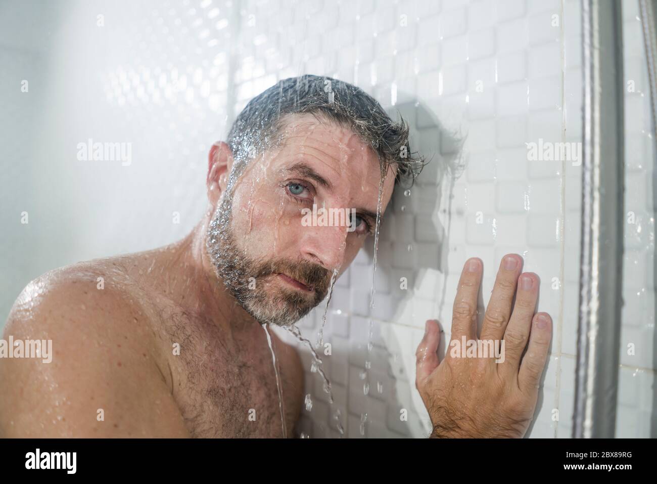 home bathroom dramatic portrait of young attractive sad and depressed man in the shower leaning
