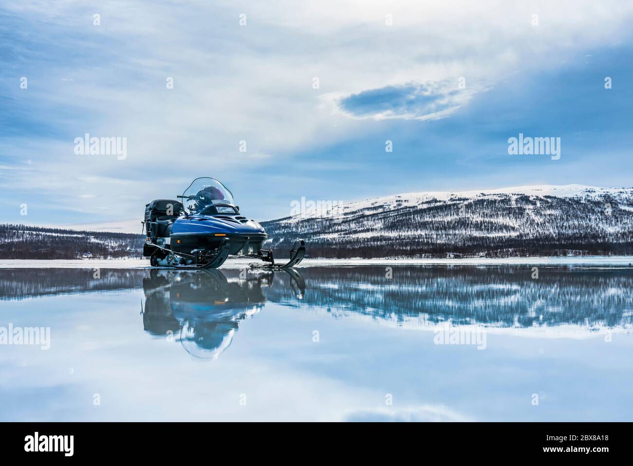 One blue snowmobile stands on a frozen lake close to open water with partially smelted ice, warm day at spring in Swedish mountains, Lappland Stock Photo