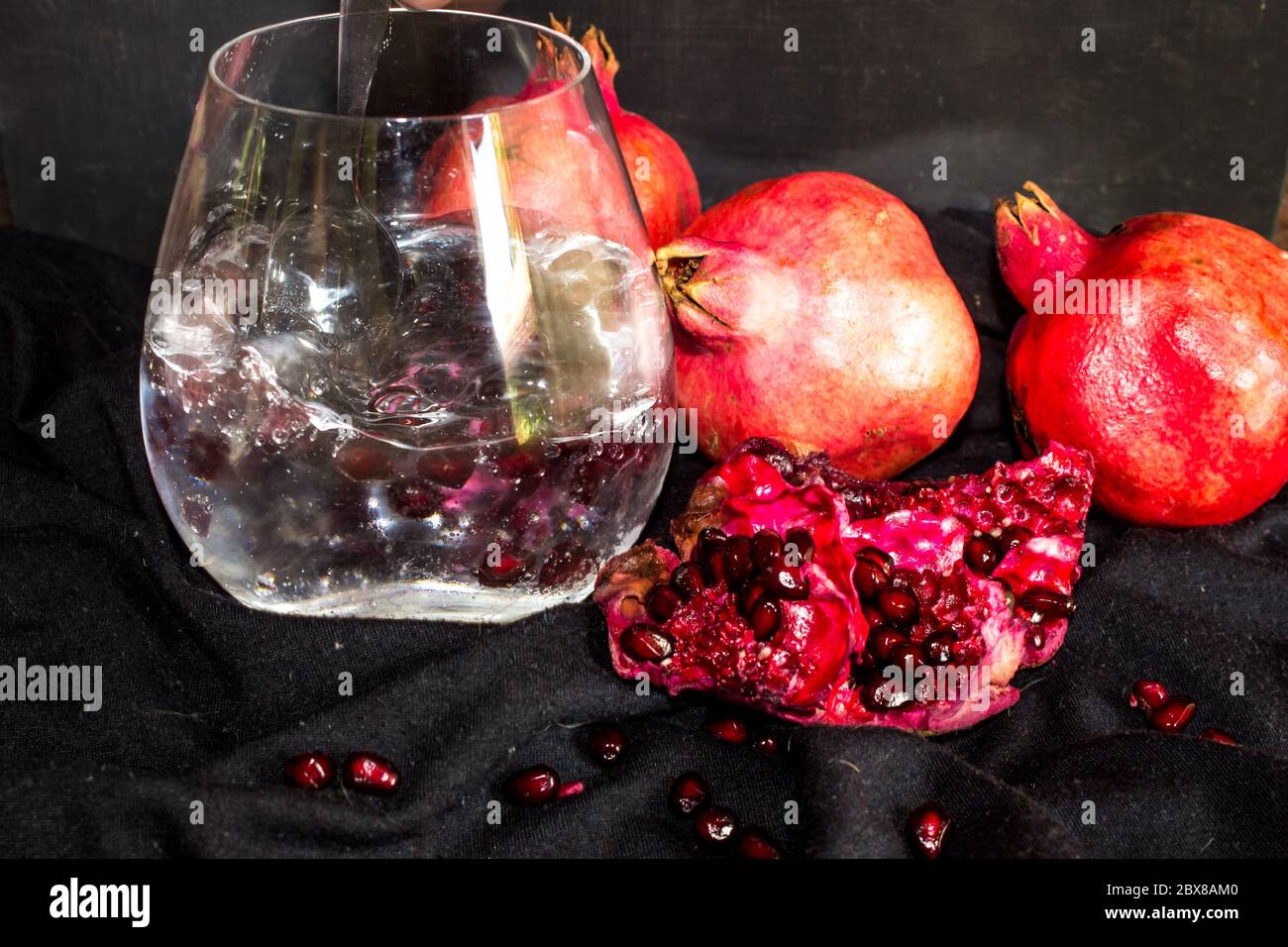 A Gin and Tonic, garnished with large amount of Pomegranate pits, with pomegranates, on a black background Stock Photo