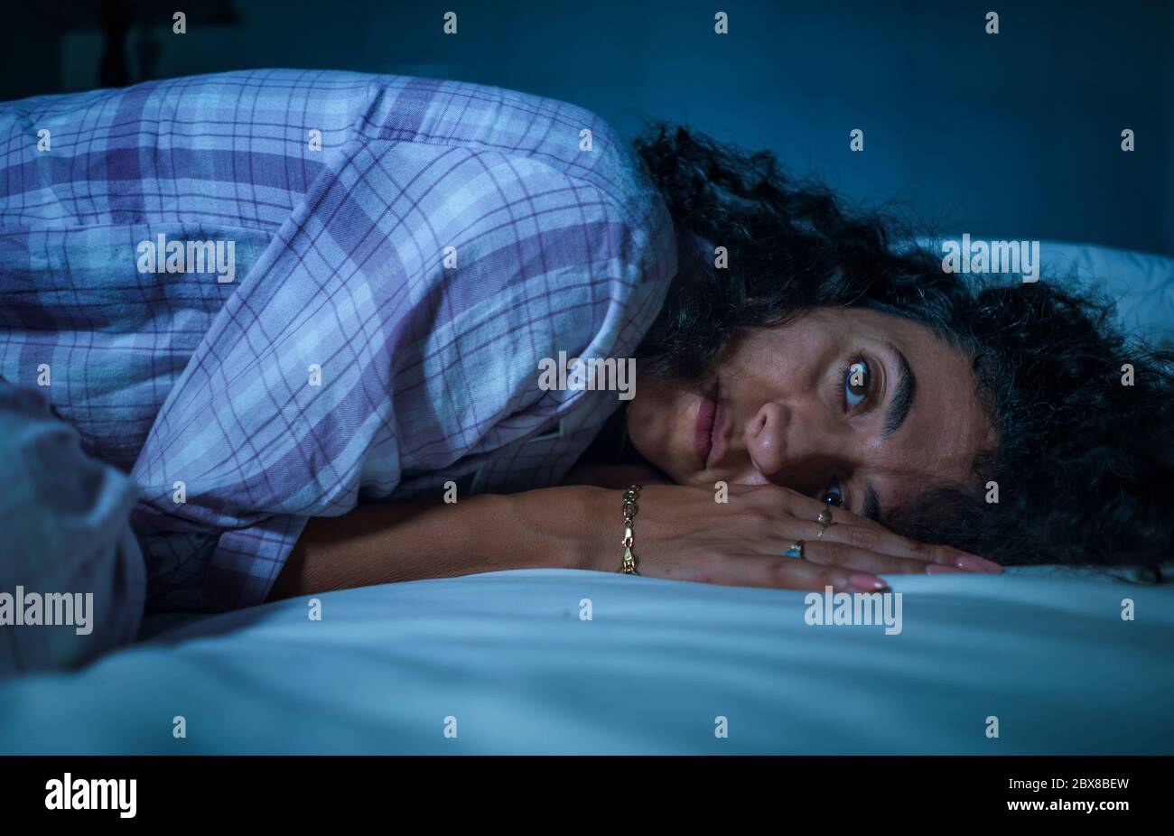 dramatic night lifestyle portrait of young sad and depressed middle eastern woman with curly hair sleepless in bed awake and thoughtful feeling worrie Stock Photo