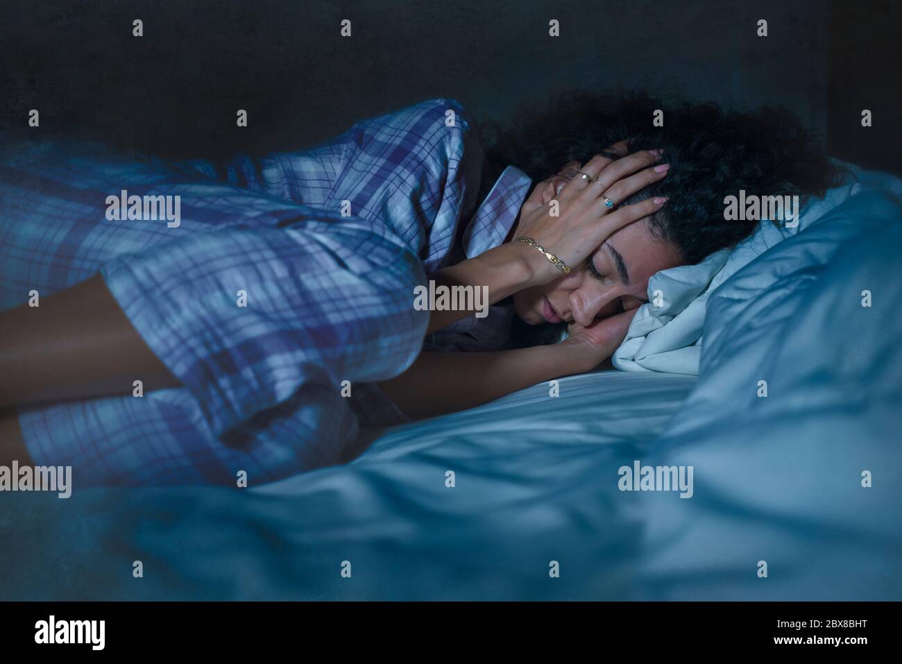 dramatic night lifestyle portrait of young sad and depressed middle eastern woman with curly hair sleepless in bed awake and thoughtful feeling worrie Stock Photo