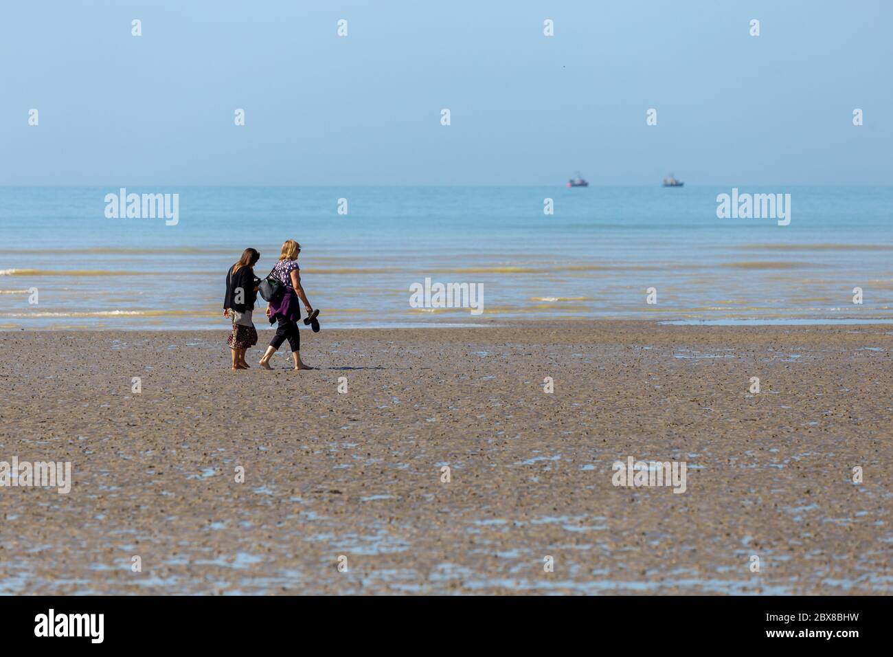 Worthing, Sussex, UK; 25th May 2020; Two Women Walking Along The Seashore.  Two Fishing boats Can Be Seen on the Horizon Stock Photo