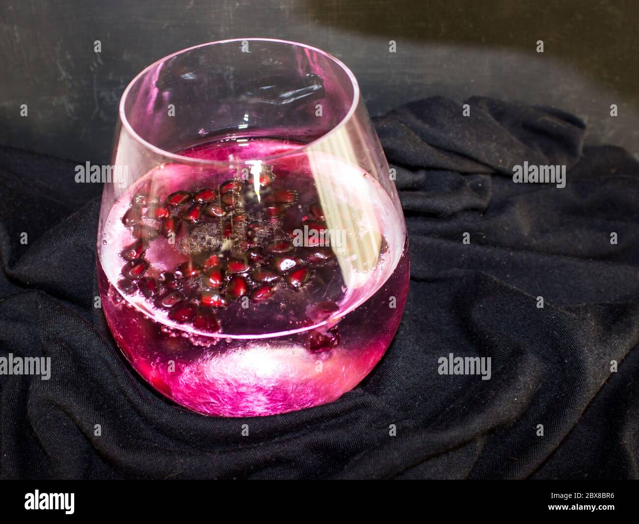 A red Pomegranate, Gin and Tonic, garnished with large amount of Pomegranate pits, on a black background Stock Photo