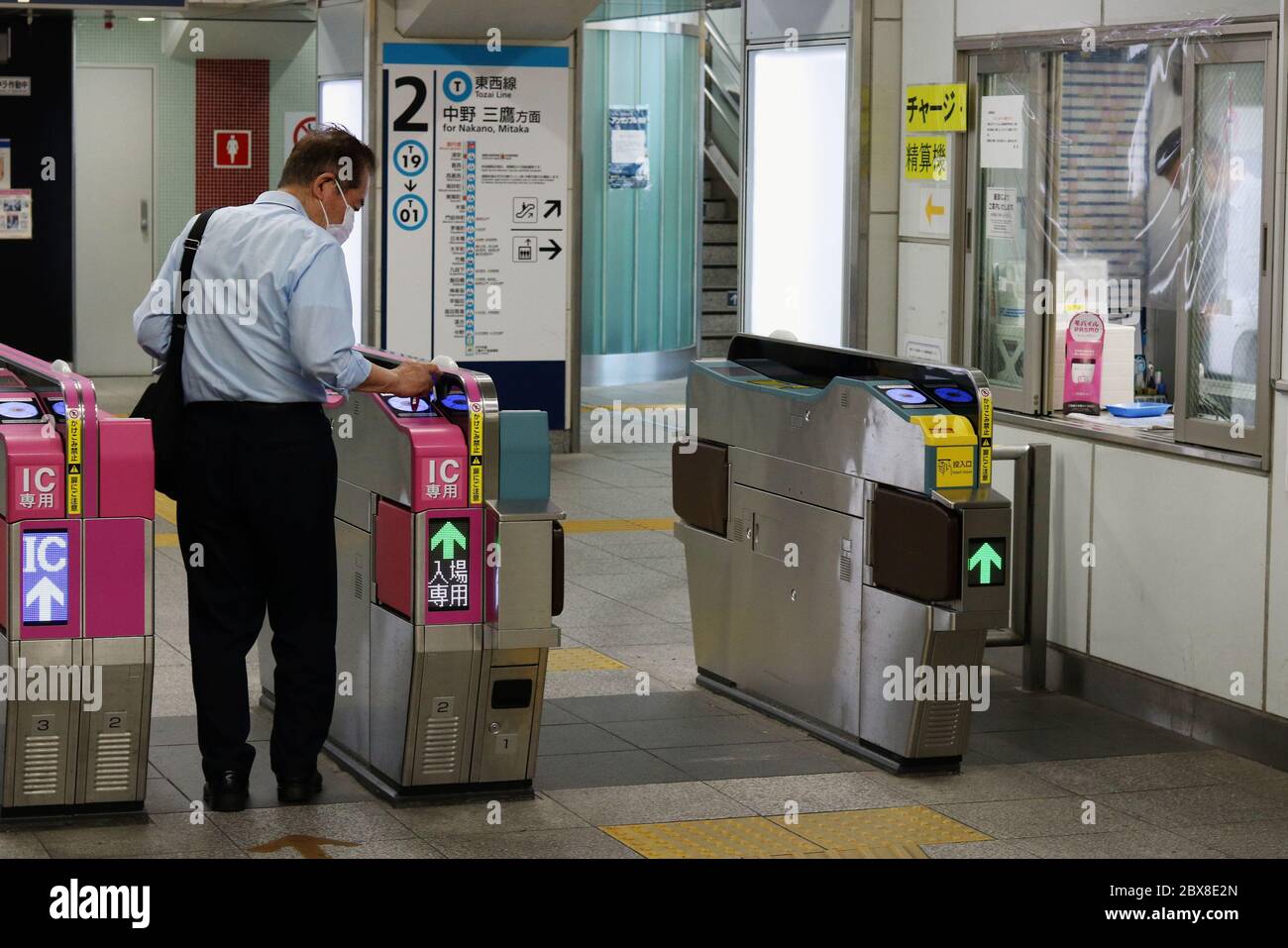 Passenger uses IC card ticket gate at Tozai Line station. People wear face masks & a plastic shield covers the ticket gate window due to  coronavirus. Stock Photo