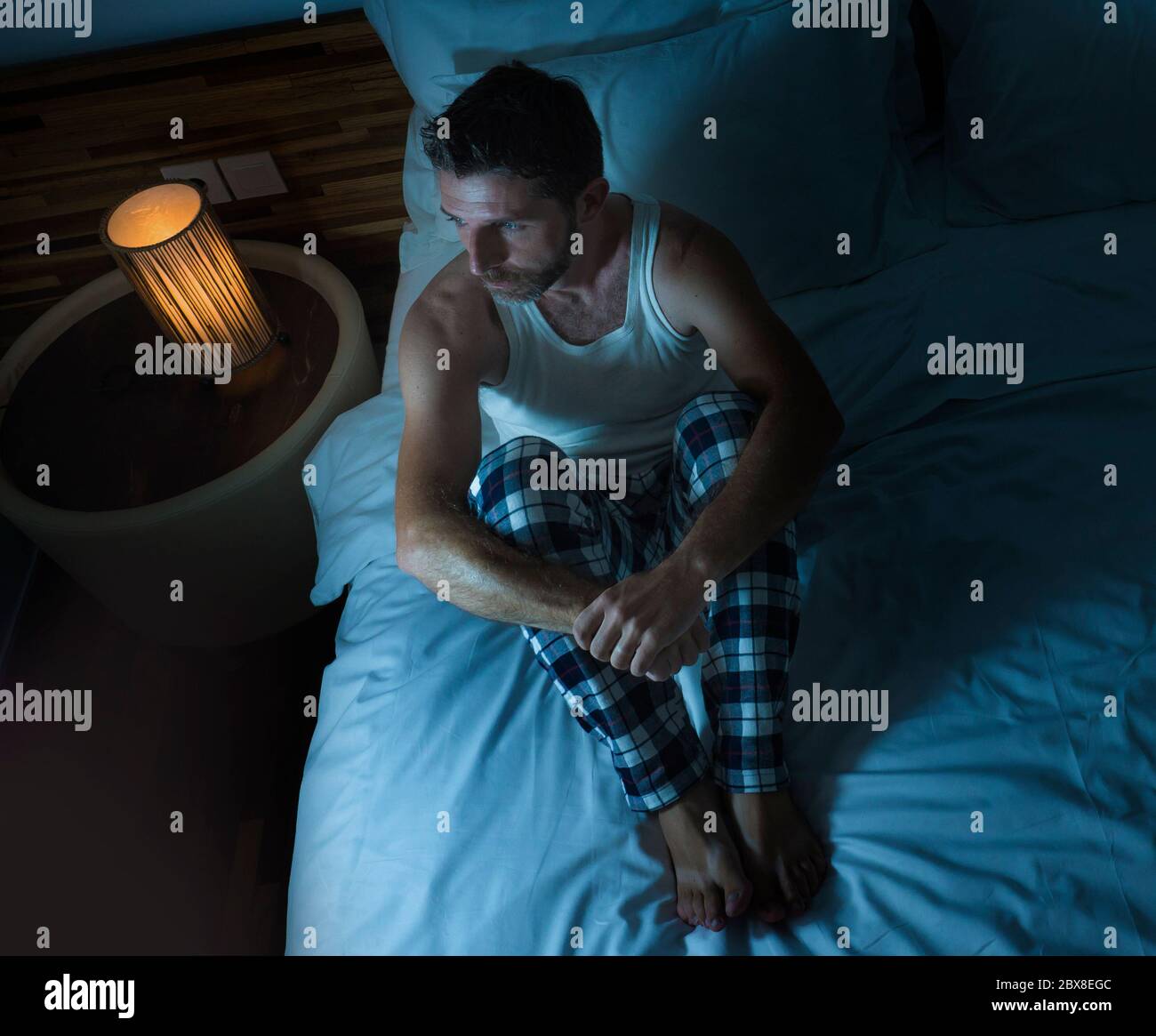 dramatic lifestyle portrait of young attractive sad and depressed man sitting on bed awake at night feeling stressed and desperate suffering depressio Stock Photo