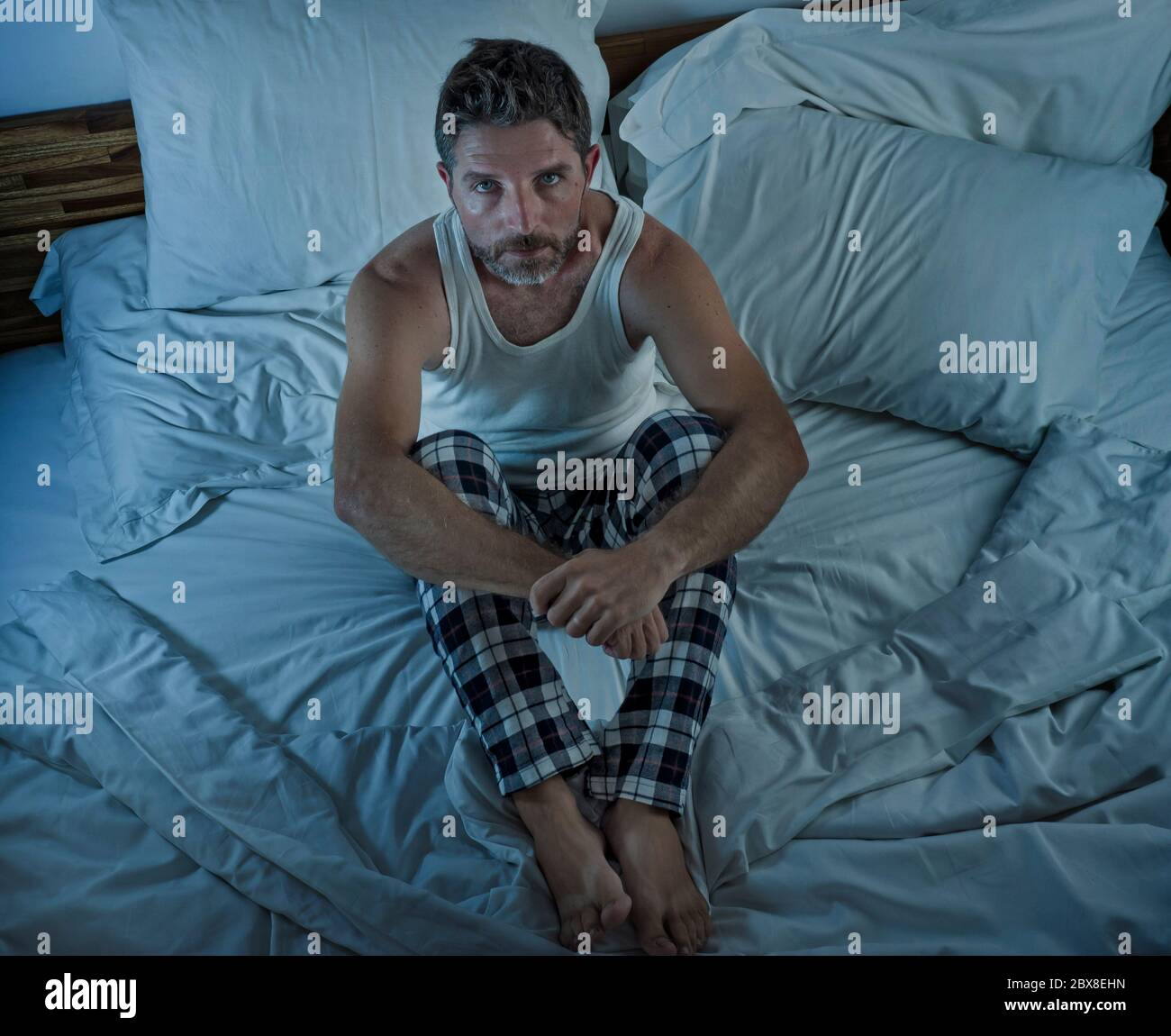 dramatic lifestyle portrait of young attractive sad and depressed man sitting on bed awake at night feeling stressed and desperate suffering depressio Stock Photo