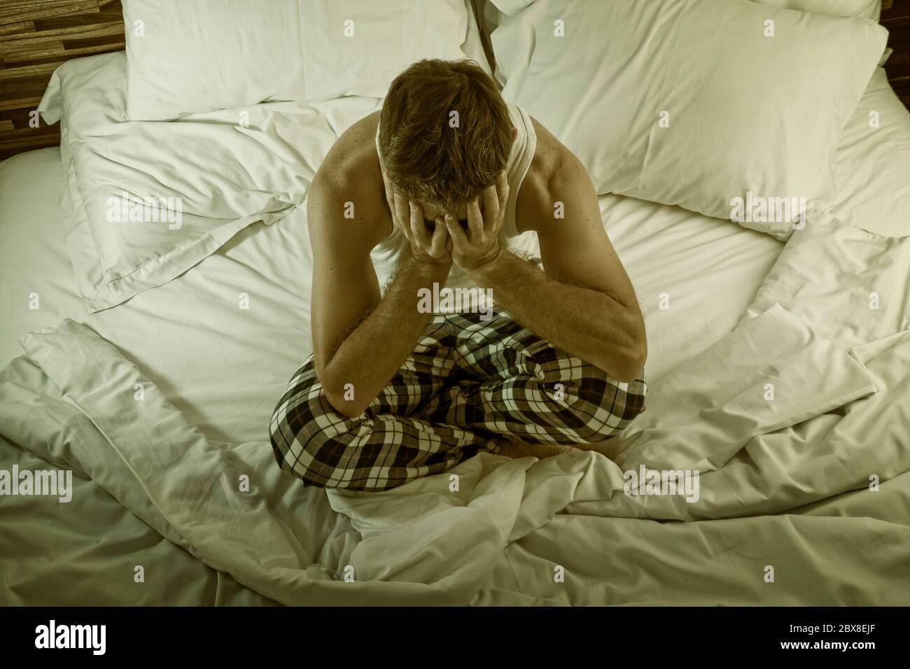 dramatic lifestyle portrait of young attractive sad and depressed man sitting on bed awake at night feeling stressed and desperate suffering depressio Stock Photo