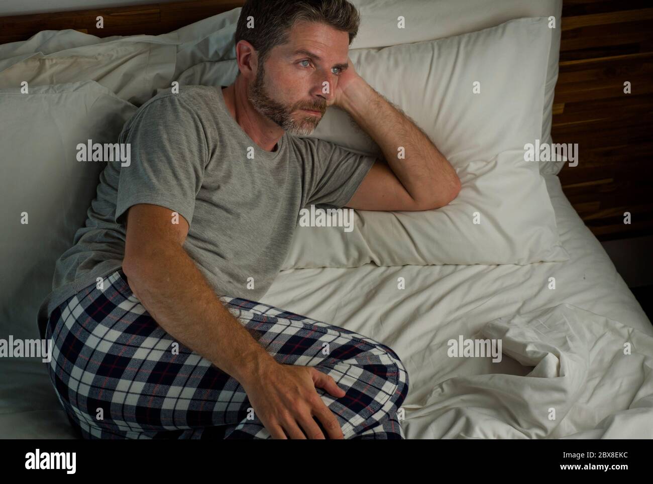 dramatic lifestyle portrait of young attractive sad and depressed man sitting on bed awake at night feeling stressed and desperate suffering depressio Stock Photo