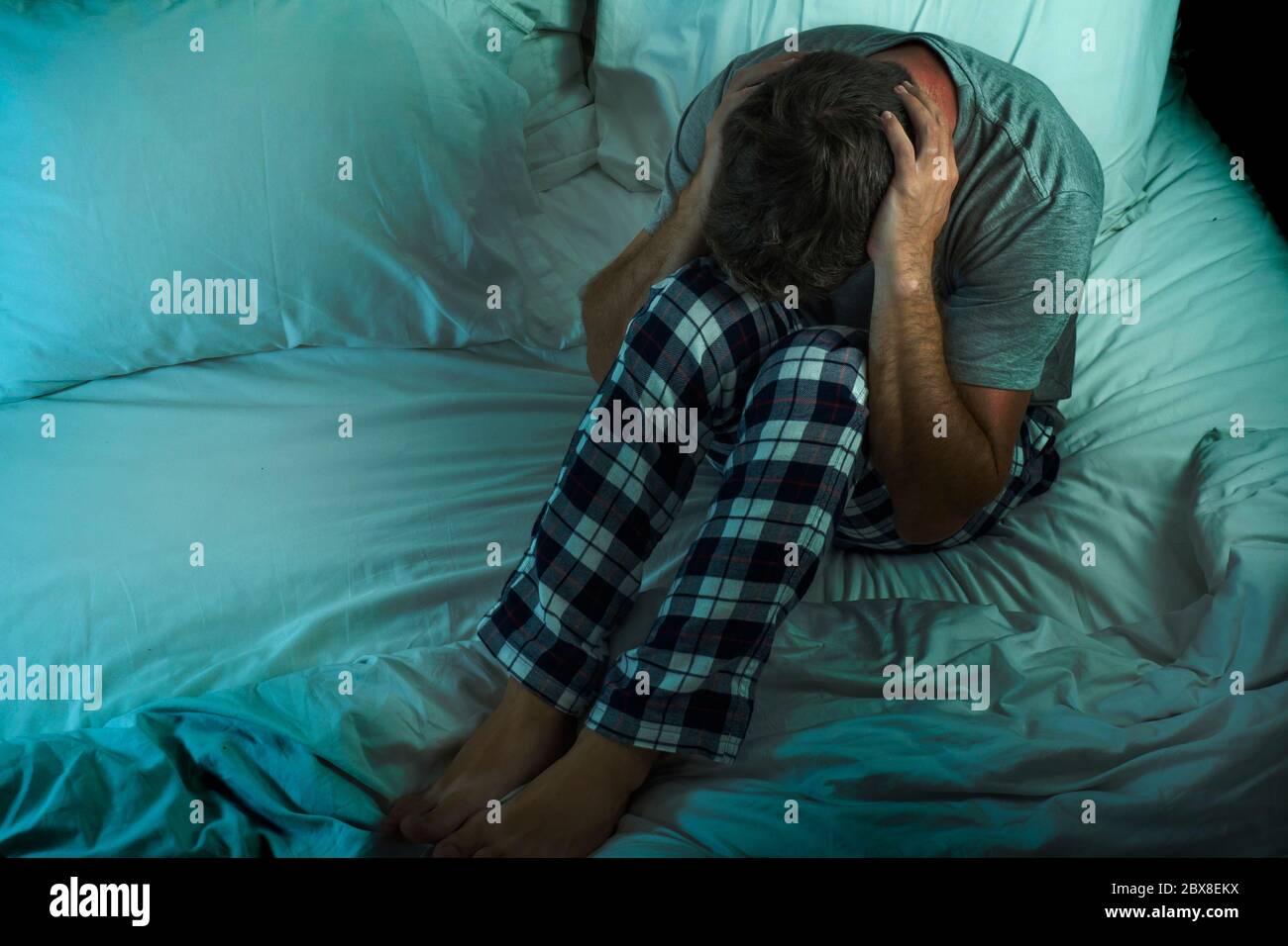 dramatic lifestyle portrait of young attractive sad and depressed man sitting on bed awake at night feeling stressed and desperate suffering depressio Stock Photo