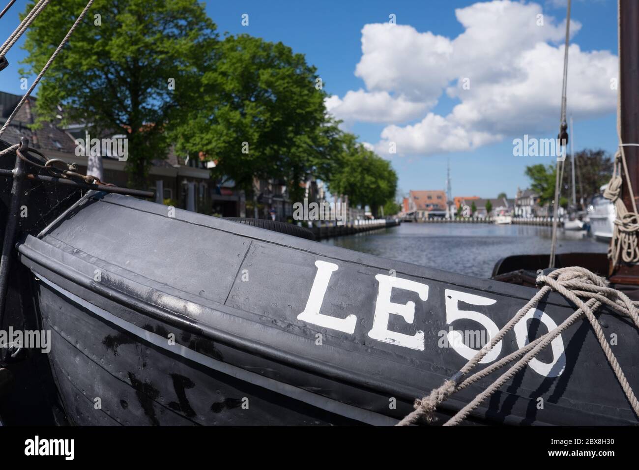 Canal with Lemsteraak LE50 in foreground, boats and houses mirrored in water in the center of  Lemmer near IJsselmeer in Friesland, Netherlands. Stock Photo