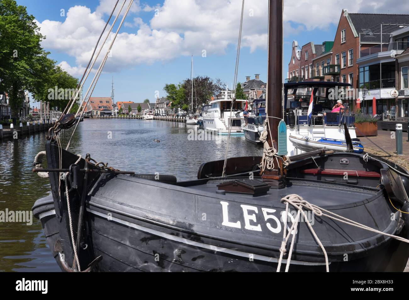Canal with Lemsteraak LE50 in foreground, boats and houses mirrored in water in the center of  Lemmer near IJsselmeer in Friesland, Netherlands Stock Photo