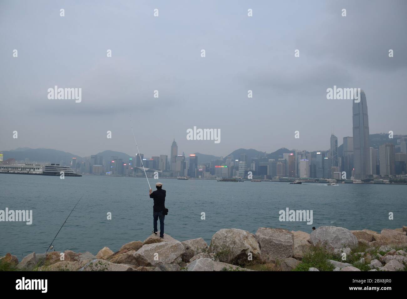 Local man fishing in West Kowloon park in front of Victoria harbour in Hong Kong island - Hong Kong Stock Photo