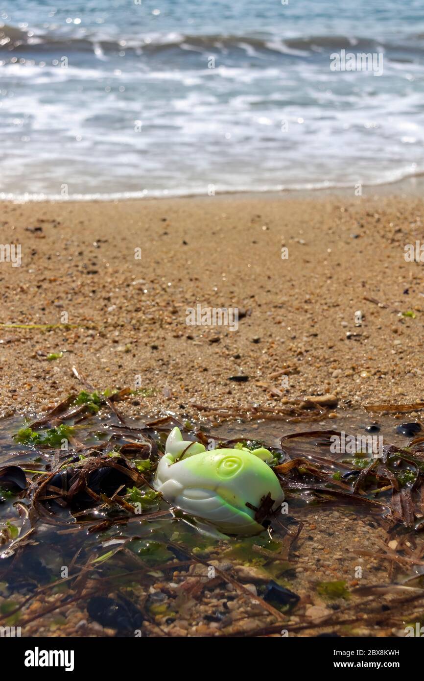 Plastic toy fish on ocean beach, water pollution Stock Photo