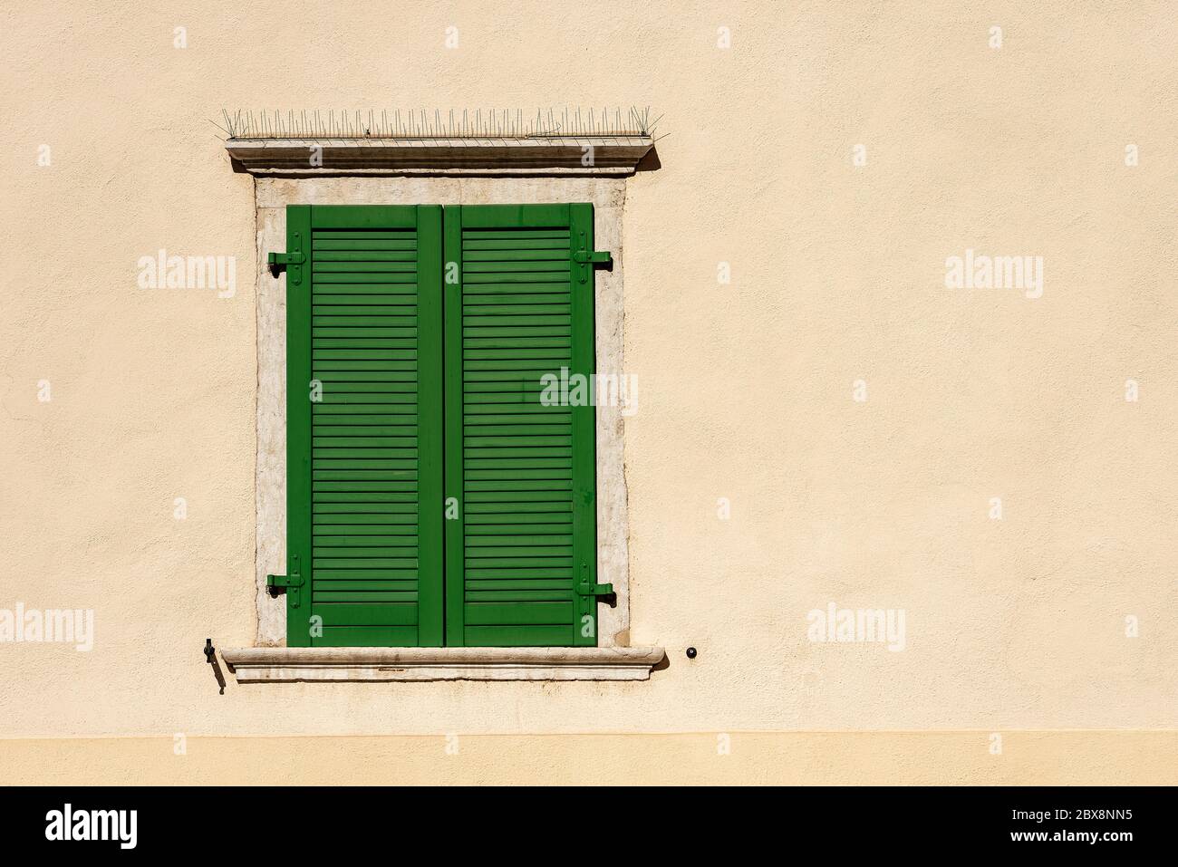 Close-up of a window with closed green wooden shutters with spike steel sticks to prevent birds from stopping, especially pigeons. Stock Photo