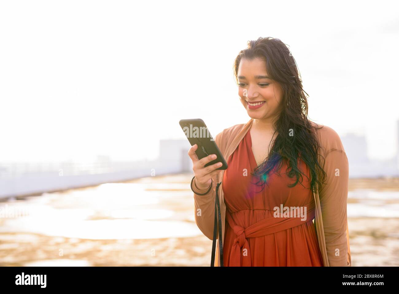 Happy young beautiful Indian woman using phone at rooftop of the ...