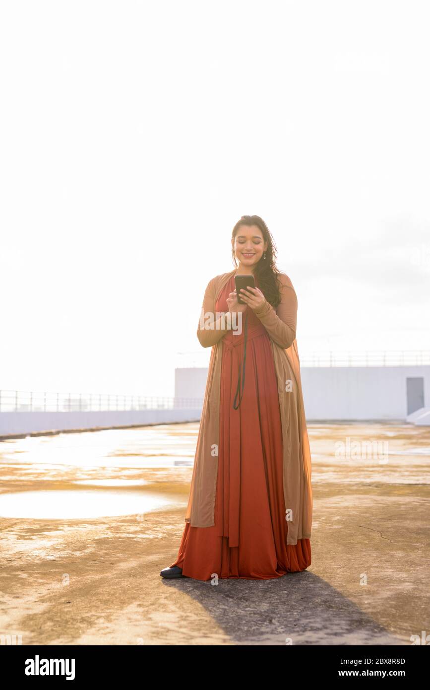 Full body shot of happy young beautiful Indian woman using phone at ...