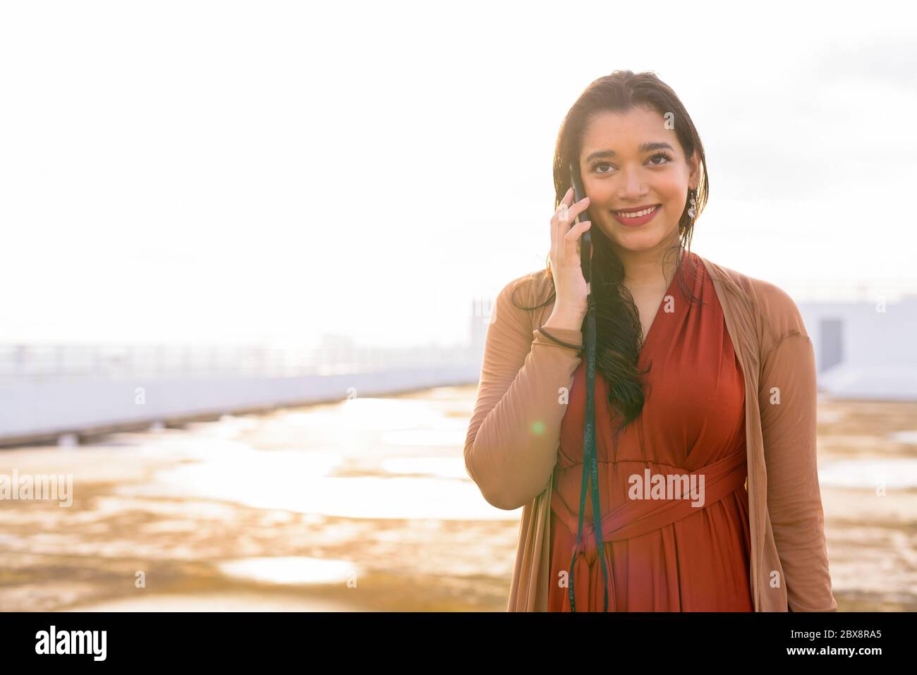 Happy young beautiful Indian woman talking on the phone at rooftop of ...
