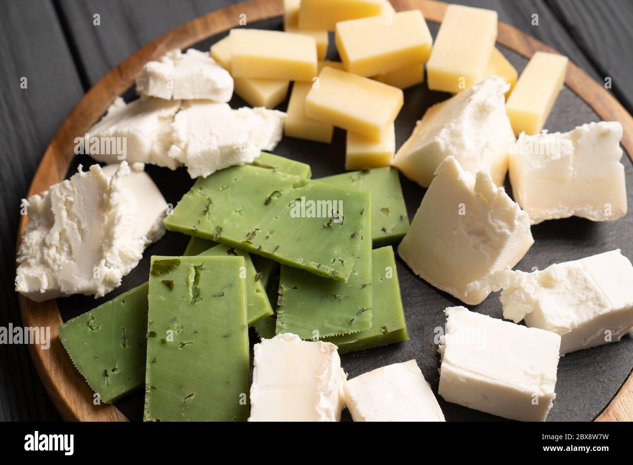 Various types of colorful cheeses diced on plate on wooden table. Top view of white, yellow and green cheese Stock Photo