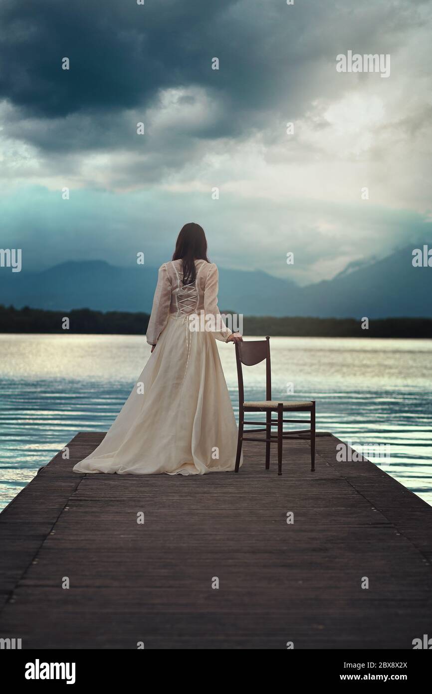 Lone and sad woman waiting on lake pier Stock Photo