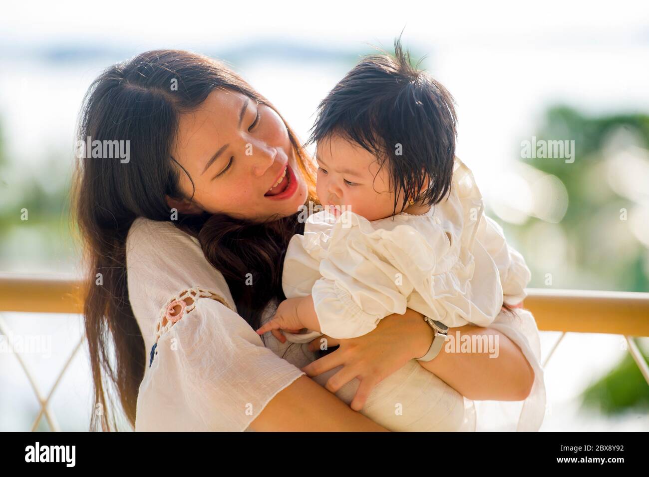 young happy and beautiful Asian Korean woman playing and holding sweet adorable baby girl sitting at holidays resort enjoying summer vacation trip in Stock Photo