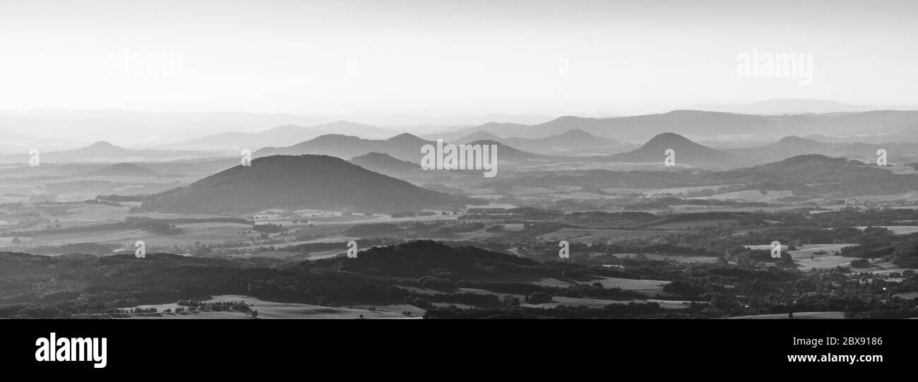 Silhouettes of volcanic hills of Ceske Stredohori, Central Bohemian Uplands, on sunny and hazy day. Czech Republic. Black and white image. Stock Photo