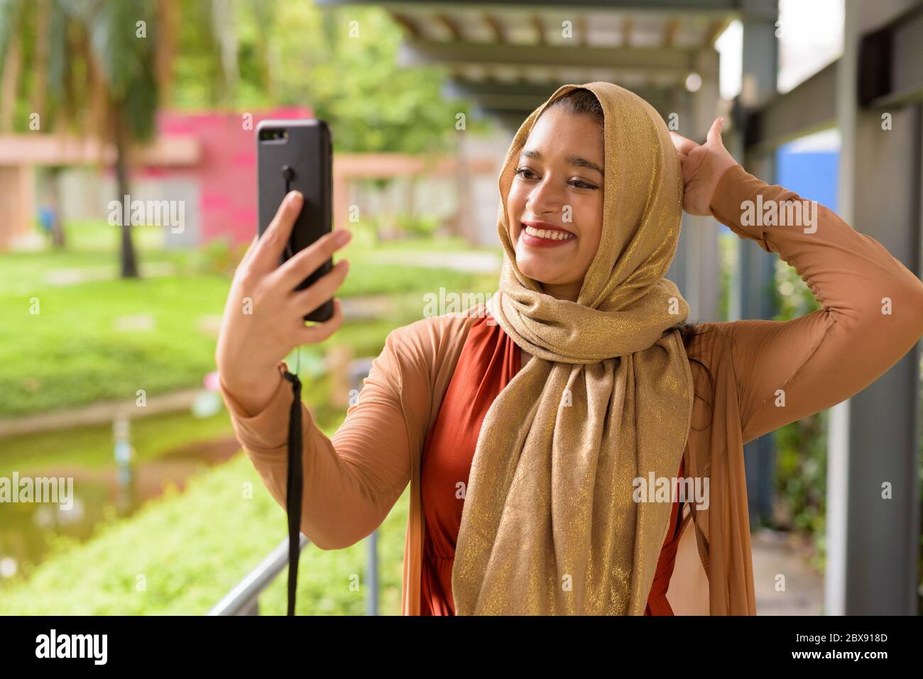 Happy young beautiful Indian Muslim woman taking selfie at the park ...