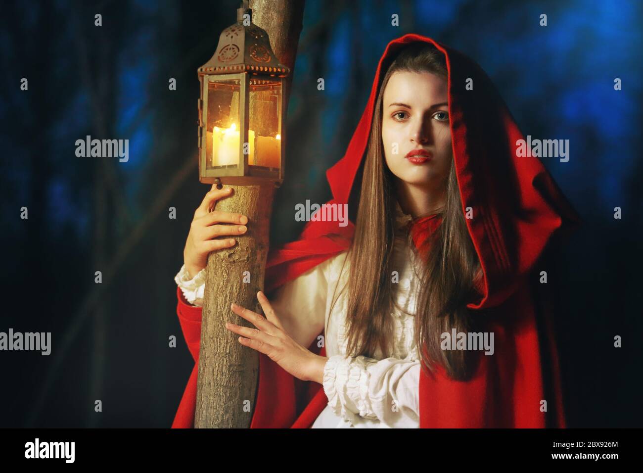 Little Red riding hood lighted by a lantern in the dark forest Stock Photo