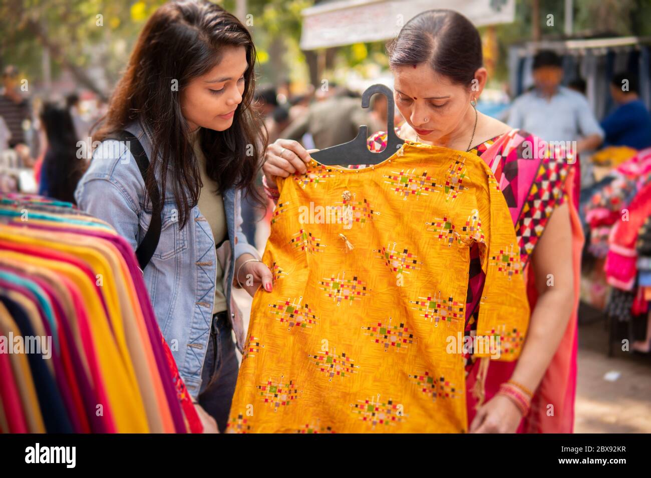 mother and daughter shopping together for clothes at outdoor street market. Stock Photo