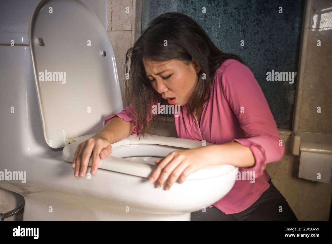 young drunk or pregnant Asian woman vomiting and throwing up in toilet WC feeling unwell and sick suffering stomach ache and nausea as pregnancy sympt Stock Photo