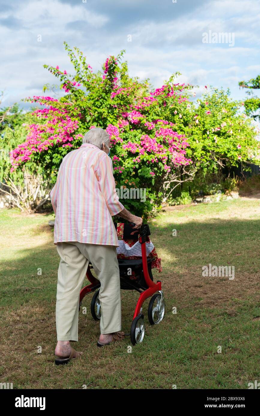 Elderly lady wearing mask getting exercise going for a walk in the garden Stock Photo