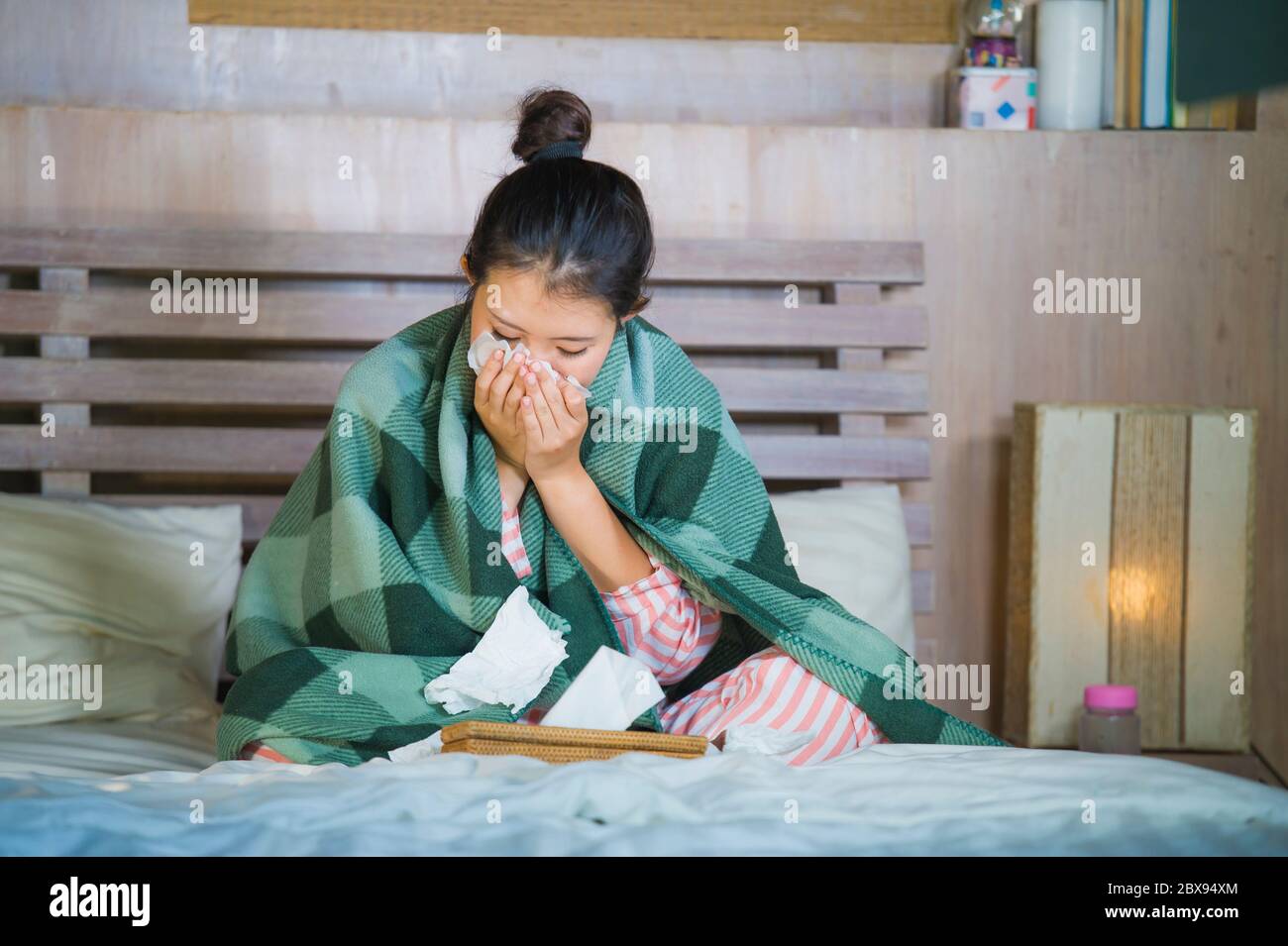 young beautiful and sweet Asian Korean girl in pajamas sick at home bedroom suffering cold and flu taking temperature with thermometer in bed blowing Stock Photo